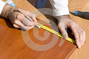 Carpenter measures the distance using a measure and marks with a carpenter`s pencil.