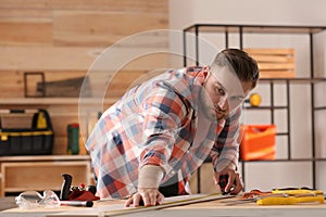Carpenter measuring wooden plank at table in workshop