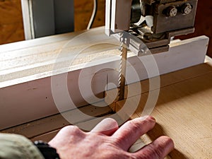 Carpenter with a missing finger cutting a piece of plywood at the bandsaw