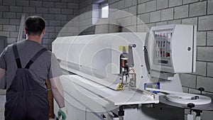 Carpenter operating on a modern edge banding machine on the factory.