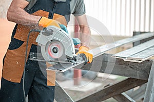 A carpenter in overalls saws a black-painted Board with a circular saw