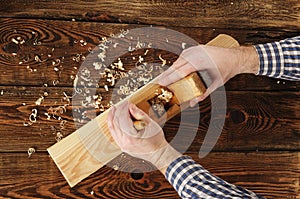 Carpenter planes a workpiece on a workbench. carpenter`s hands. old wooden plane