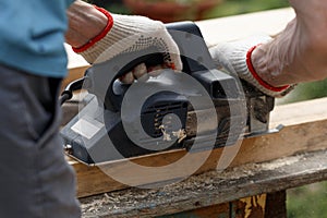 A carpenter planks wood with an electric plane. Woodworking carpentry. Close-up. Man in the garden sanding wooden planks