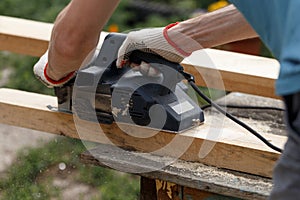 A carpenter planks wood with an electric plane. Woodworking carpentry. Close-up. Man in the garden sanding wooden planks