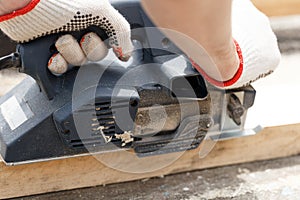 A carpenter planks wood with an electric plane. Woodworking carpentry. Close-up. Man in the garden sanding wooden planks