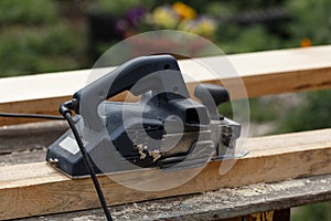 A carpenter planks wood with an electric plane. Woodworking carpentry. Close-up. Man in the garden sanding wooden planks
