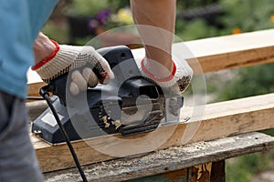 A carpenter planks wood with an electric plane. Woodworking carpentry. Close-up. Man in the garden sanding wooden planks