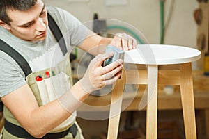 Carpenter polish round chair in workshop. Woodworker in apron