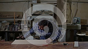 Carpenter polishes the wooden board with sandpaper on desktop. Work in the carpentry workshop