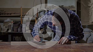 Carpenter polishes the wooden board with sandpaper on desktop. Work in the carpentry workshop