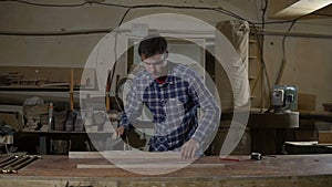 Carpenter polishes the wooden board with sandpaper on desktop. Work in the carpentry workshop