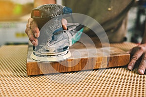 Carpenter polishes a wooden board in a workshop. The process of the grinding machine. Manufacturing of wood furniture