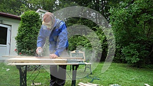 Carpenter polishing a wooden board with an electric sander in garden yard
