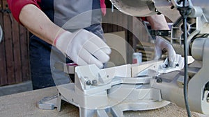 Carpenter in protective gloves cuts off wooden oak bar on mitre saw close-up