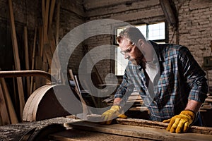 carpenter in protective gloves and googles using machine saw