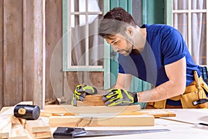 Carpenter in protective gloves using hand plane for shaping wood on porch