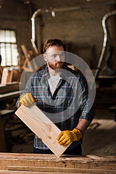 carpenter in protective gloves working with wooden plank