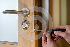 Carpenter repairing door lock. Installing a door handle. Handyman tightening door hinge . Hands of the repairman with a