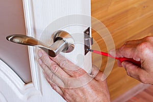 Carpenter repairs the front door lock. fastens the handle with a screwdriver