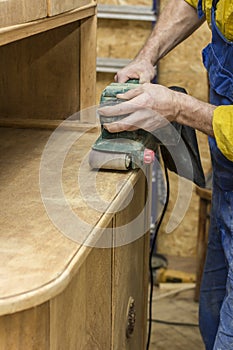 Carpenter restores vintage a sideboard by an electric of the grinding machine.