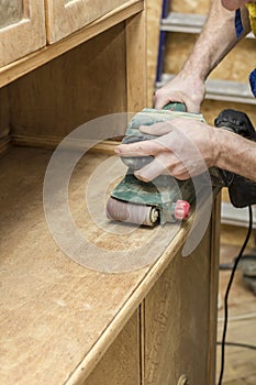 Carpenter restores vintage a sideboard by an electric of the grinding machine.