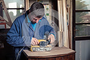 Carpenter restoring furniture with belt sander