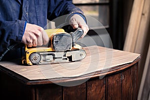 Carpenter restoring furniture with belt sander