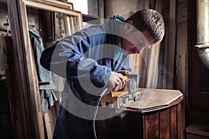 Carpenter restoring furniture with belt sander