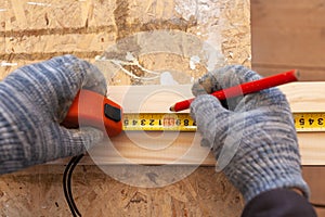 Carpenter`s hands with tape measure and cardash making a mark on the board