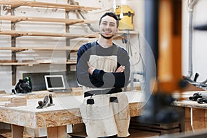 Carpenter`s portrait in work clothes in front of workbench. Portrait of smiling man at work in carpenter workshop. startup