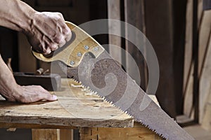 Carpenter sawing a board with a hand wood saw