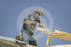 Carpenter sawing board on roof