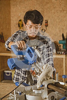 Carpenter sawing with circular saw in carpentry shop. Asian craftsman working on woodworking machines in a workplace. Cabinet