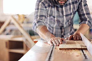 Carpenter sawing wood with a table saw in his workshop