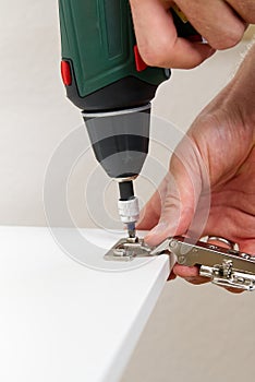 the carpenter screws the hinge on the furniture door. Furniture assembly service concept