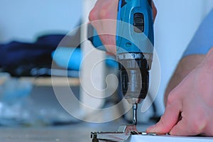 Carpenter screws hinge to furniture door using electric screwdriver, closeup.