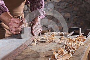 Carpenter smoothing out long wooden beam with tool