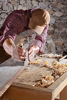 Carpenter smoothing out long wooden beam with tool