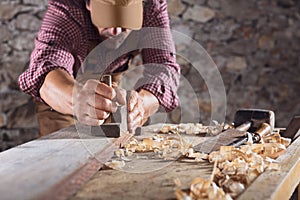 Carpenter smoothing out long wooden beam with tool