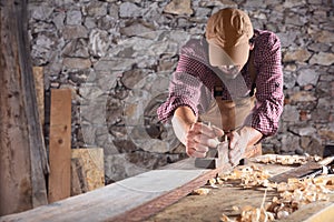 Carpenter smoothing out long wooden beam with tool photo