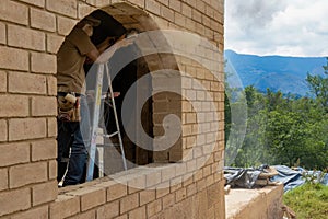 A carpenter on a step ladder grinding an adobe brick frame to accommodate a window