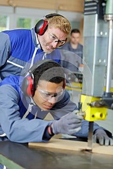 Carpenter training male apprentice to use mechanized saw