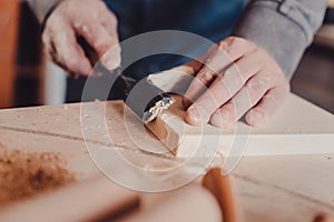 carpenter use a chisel to shapes a wooden plank.