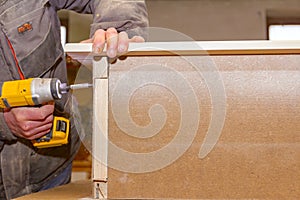 Carpenter uses hand drill, acu power tool and tightens the screws on the wooden door frame