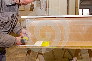 Carpenter uses hand drill, acu power tool and tightens the screws on the wooden door frame