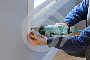 Carpenter using air nail gun to moldings for window, close up on nail gun