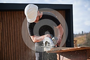 Carpenter using circular saw for cutting joist for building wooden frame house.