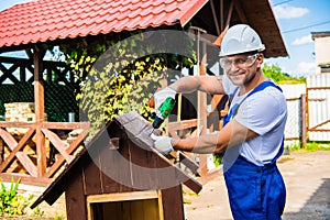 Carpenter using electric screwdriver. Man builds a roof of wooden planks of a small house. Building dog booth