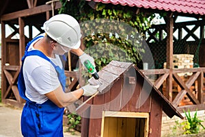 Carpenter using electric screwdriver. Man builds a roof of wooden planks of a small house. Building dog booth