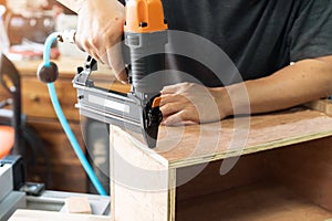 Carpenter using nail gun or brad nailer tool on wood box in a workshop ,furniture restoration woodworking concept. selective focus